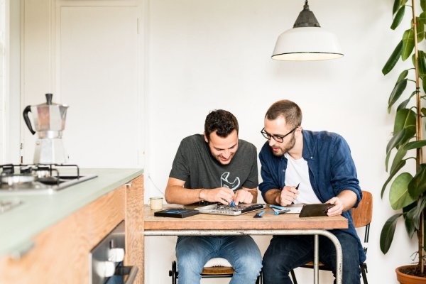 Two people sit at a table leaning over a laptop repair